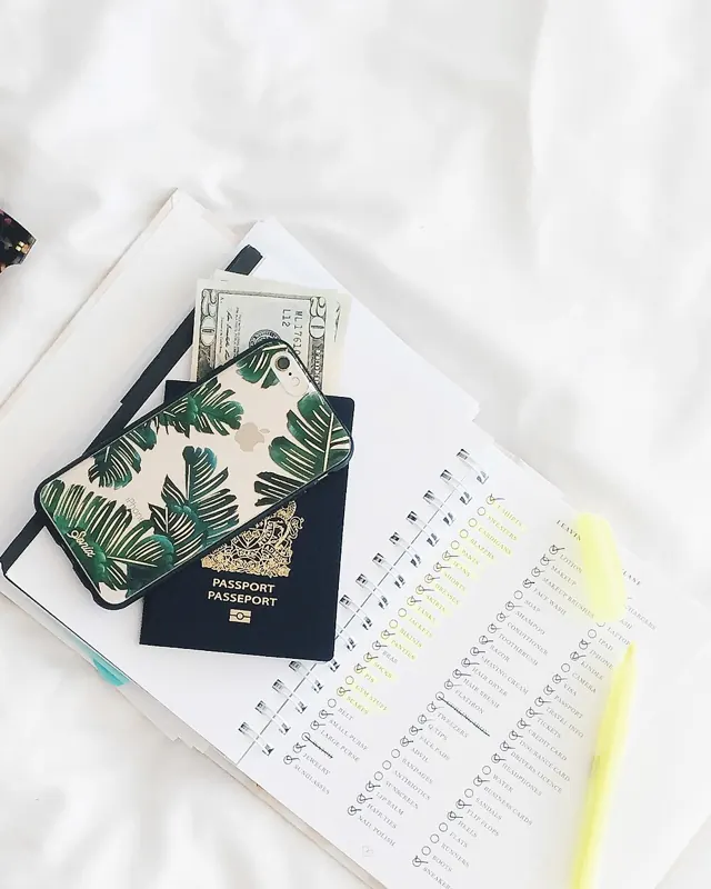 Sunglasses, a passport and a travel notebook laid out on white linen