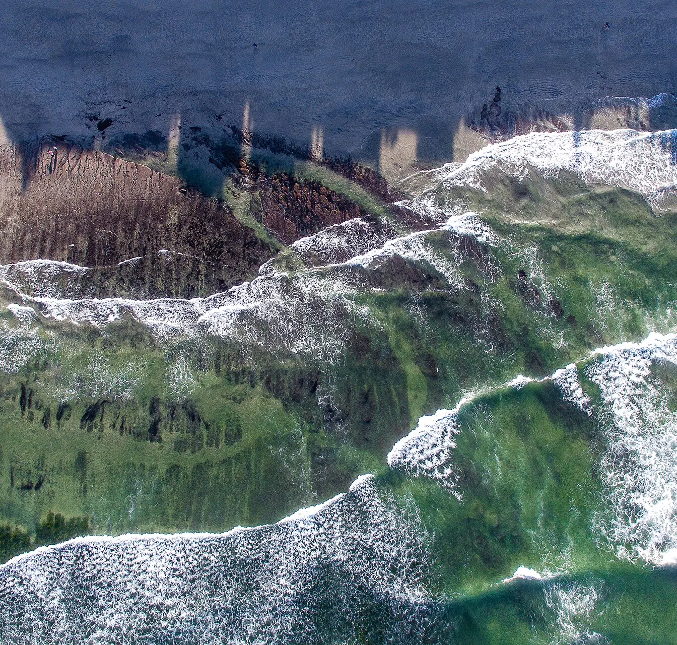 Aerial view of white surf breaking over a green-blue coastline